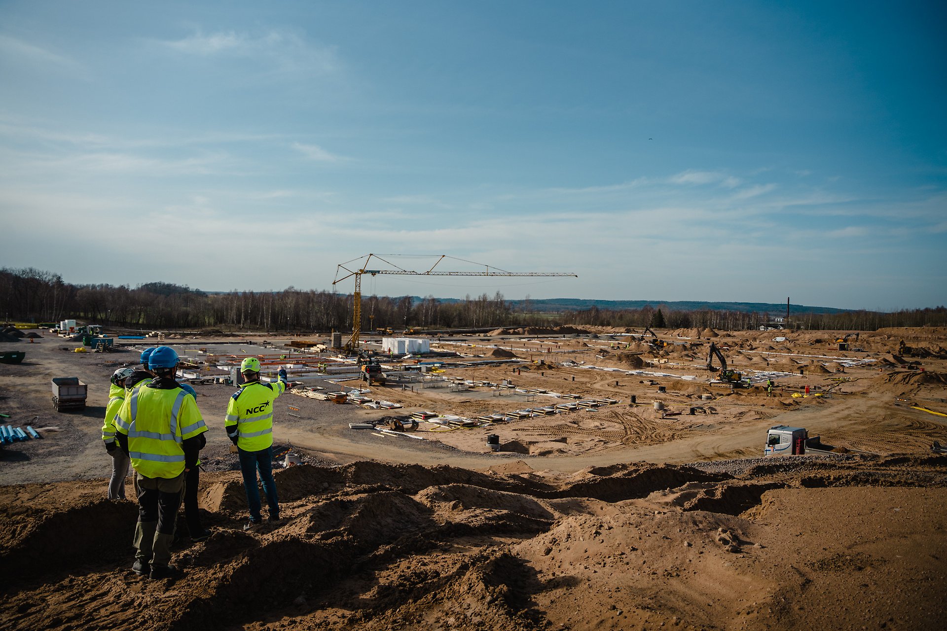 Tre projektledare står i reflexvästar och kollar ut över ett bygge. Foto: Alexander Gustavsson/Försvarsmakten