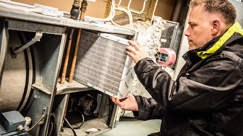 En person byter filter i ett ventilationssystem.