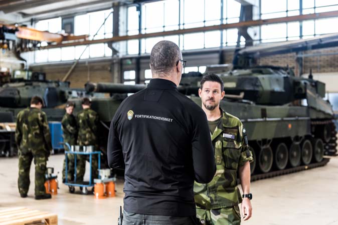 Fortverkare och militär pratar framför stridsvagn