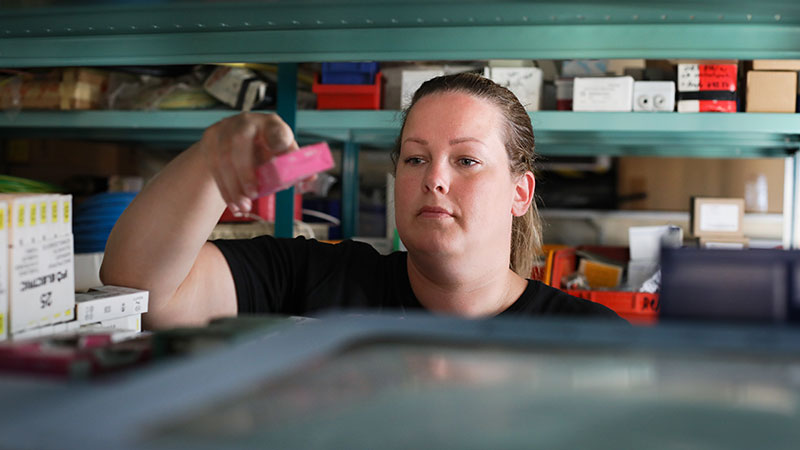 Medarbetare (tjej) plockar saker från en hyla i ett förråd. Foto: Peter Malmrup