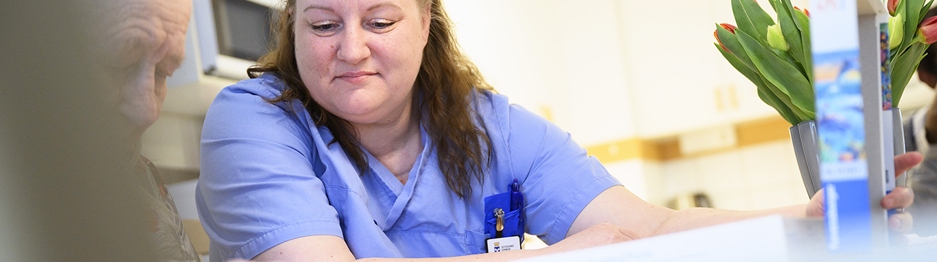 En kvinna som jobbar inom vården sitter och pratar med en äldre man.